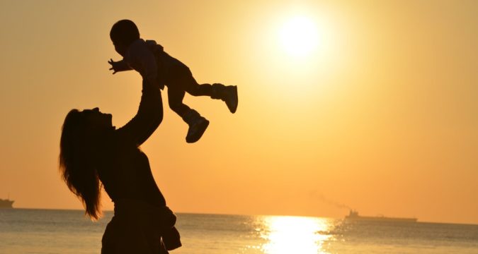 woman carrying baby at beach during sunset