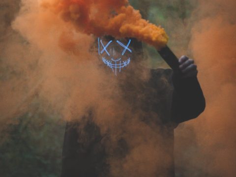 person wearing mask holding colored smoke bomb