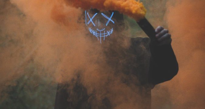 person wearing mask holding colored smoke bomb
