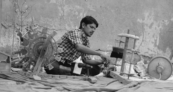 serious ethnic man weaving textile on street