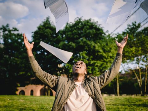 happy student throwing papers in air in park