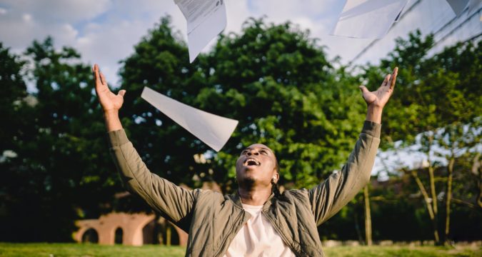happy student throwing papers in air in park